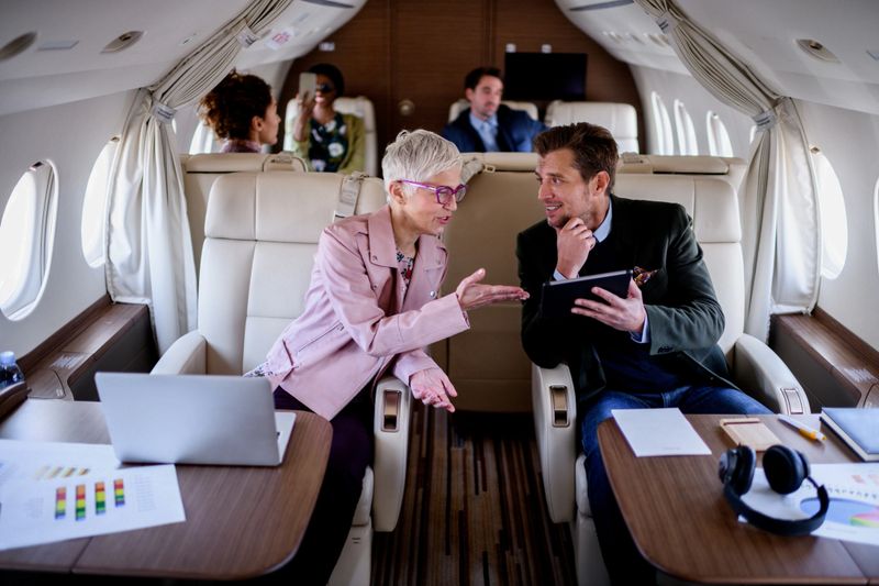 Group of people traveling by private jet airplane. Couple in front view is having business meeting.