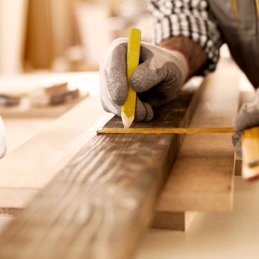 A person marking measurements on wood using a pencil and ruler.
