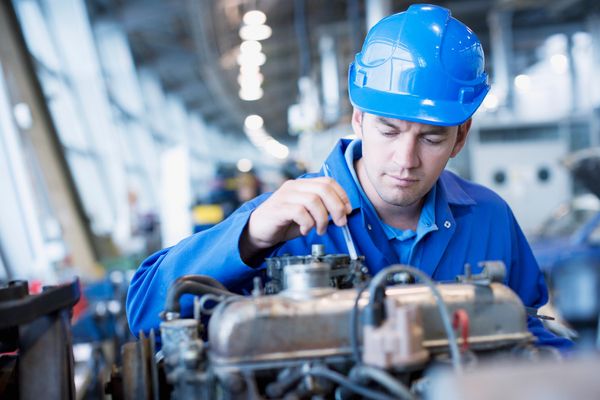 Engineer in blue uniform working on a machine in a factory.