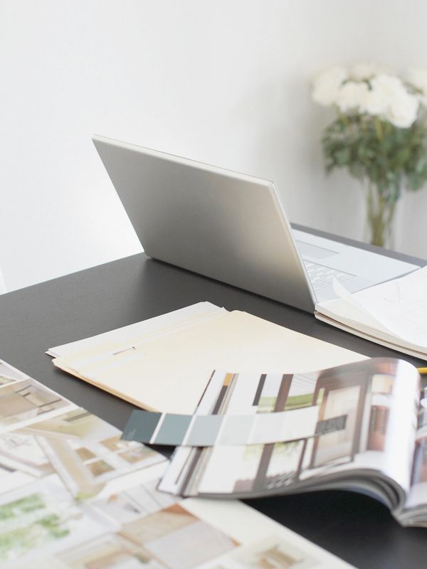 Workspace with a laptop, documents, and a flower vase in the background.
