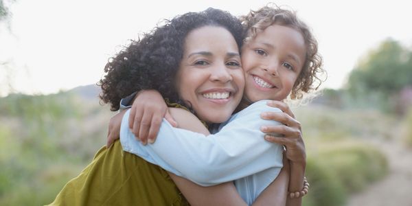 A joyful mother and child hugging outdoors in natural light.
