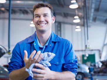 Smiling mechanic cleaning hands with rag in workshop.