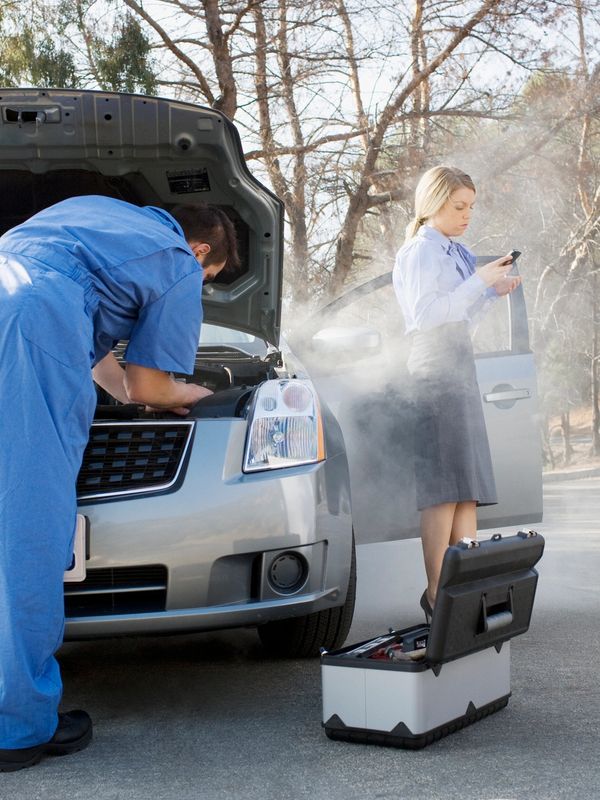 Mechanic fixing a steaming car while woman uses phone.