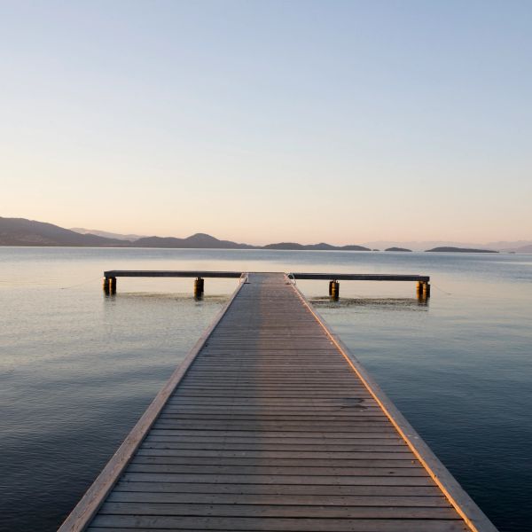 Wooden pier extending into calm lake at sunset with distant mountains.