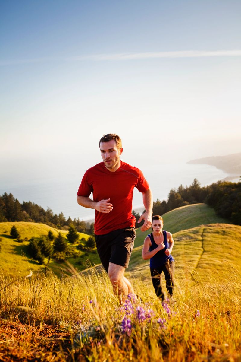 Man and woman running along grassy trail at sunset.