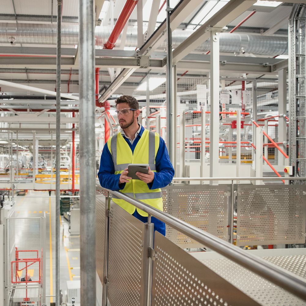 Factory worker in safety vest holding tablet and inspecting facility.