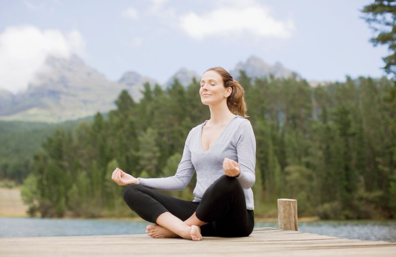 Woman practicing yoga on pier by lake