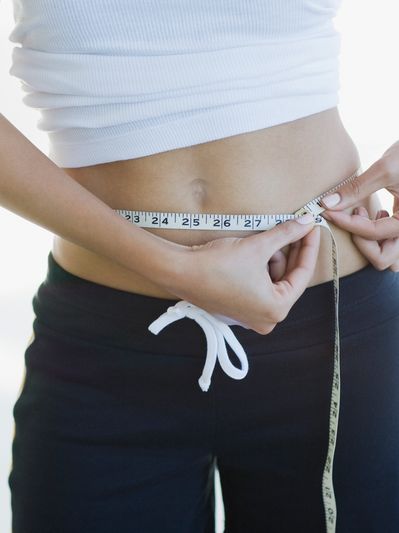Person measuring their waist with a tape measure.
