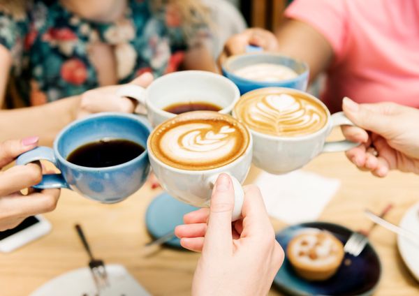 Friends clinking coffee cups in a cheerful toast.