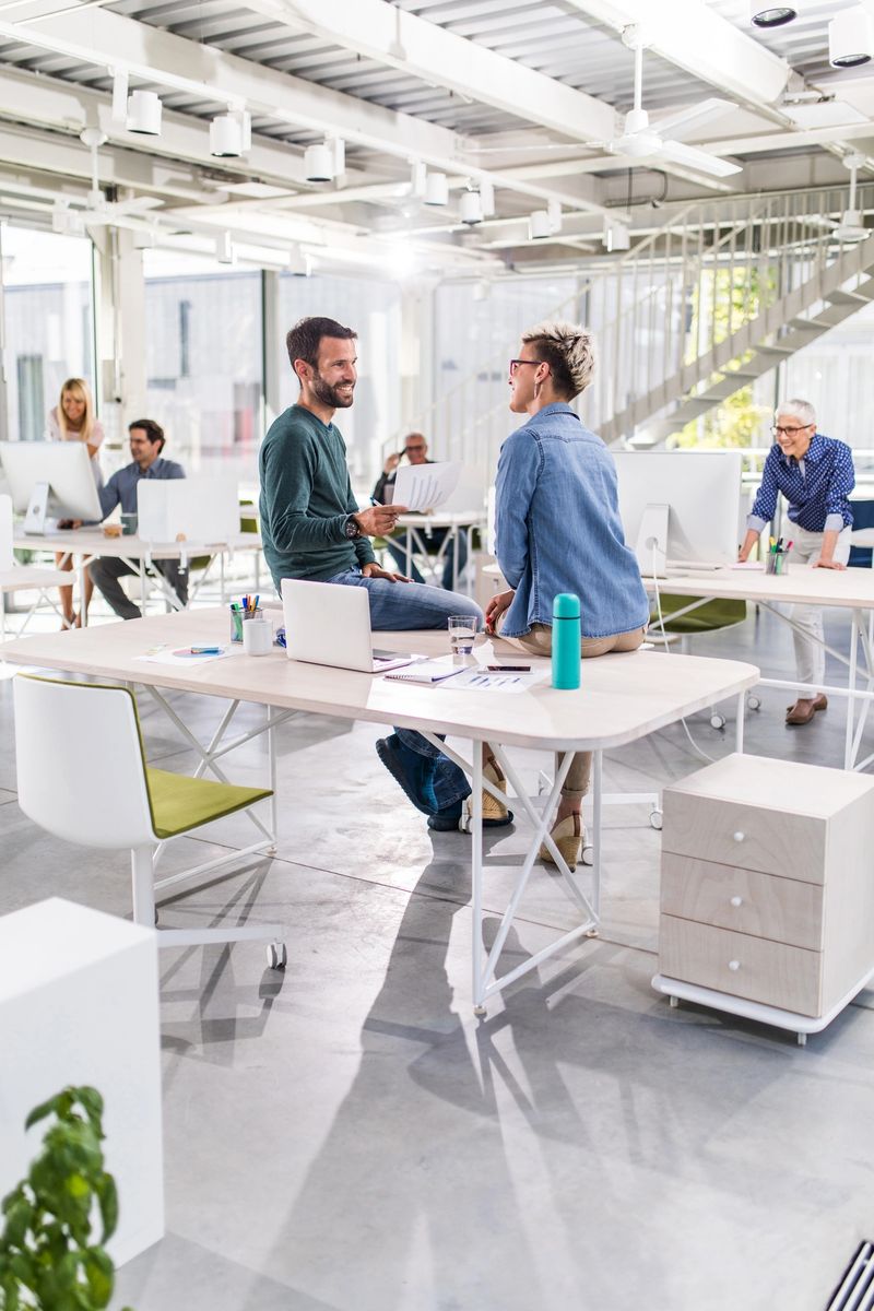Happy businessman cooperating with his female colleague while talking about new business reports in the office. There are people in the background.