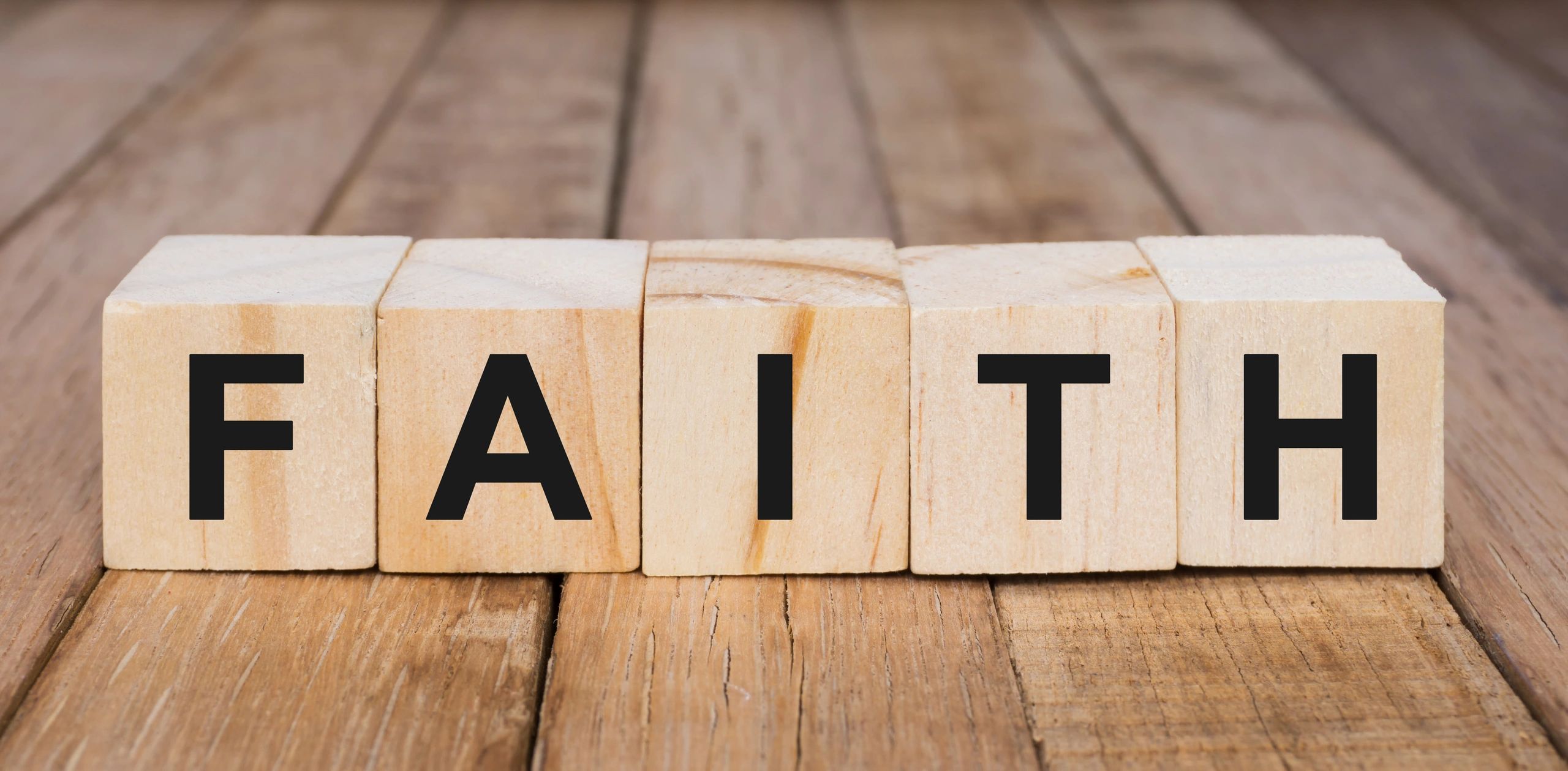 Wooden blocks spelling the word 'FAITH' on a wooden surface.