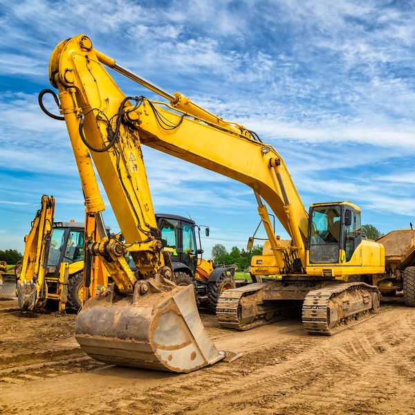 Yellow excavators parked on a construction site under a blue sky.