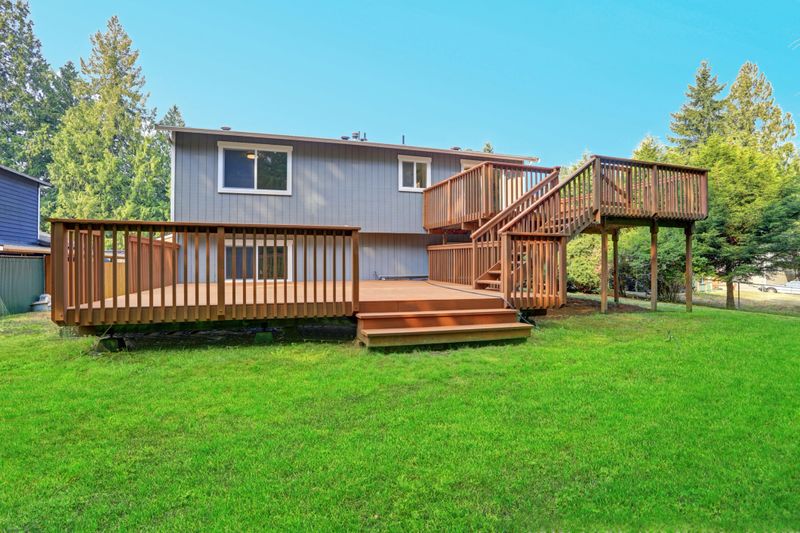 Backyard view of grey rambler house with upper and lower decks and green lawn. Kirkland, WA, USA.