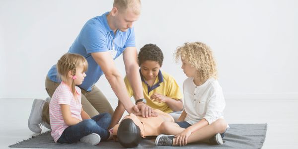 An adult teaching children CPR on a mannequin.