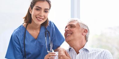 A nurse in blue scrubs smiles warmly with an elderly man.
