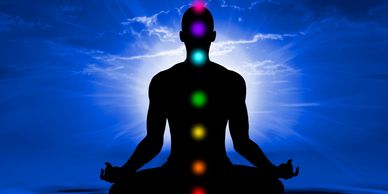 Outline of a person sitting with illuminated chakras in a meditating pose with a dark blue sky. 