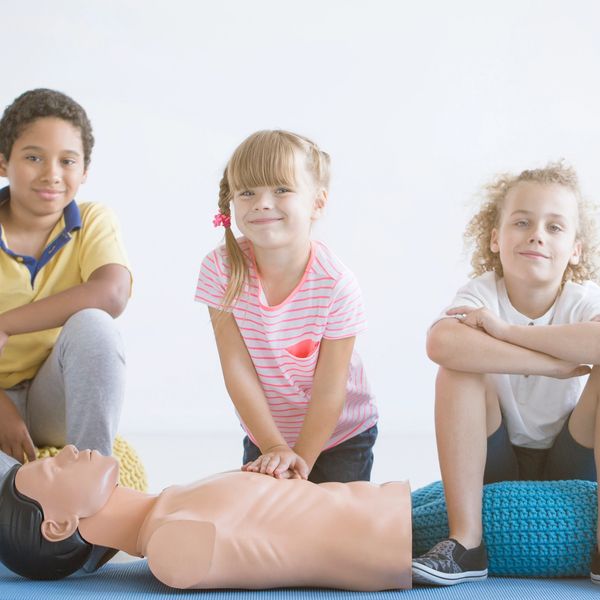 Children practicing CPR on a training mannequin in a bright room.