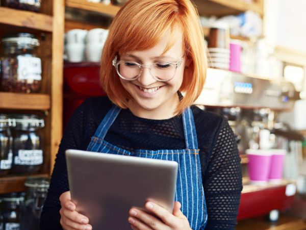 Smiling barista in apron using a tablet in a cozy café.