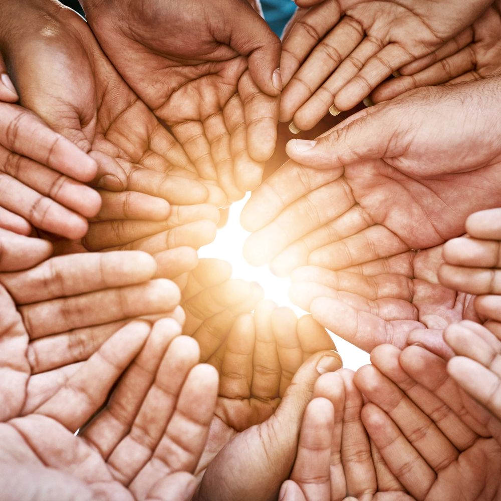 Multiple hands forming a circle around bright light symbolizing unity.