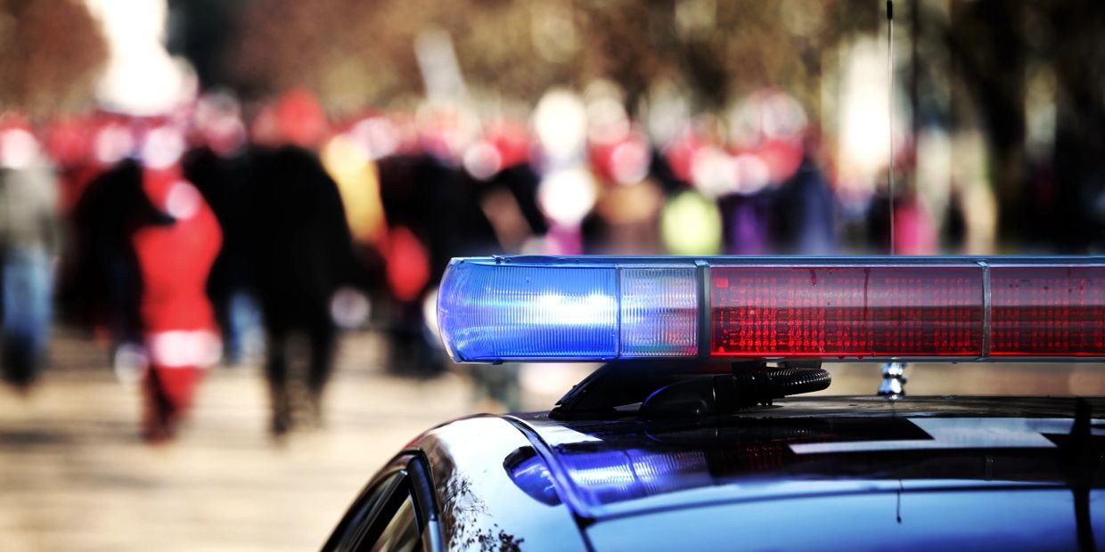 Police car with flashing lights in front of a crowd.