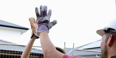Two construction workers in safety gear giving a high-five.