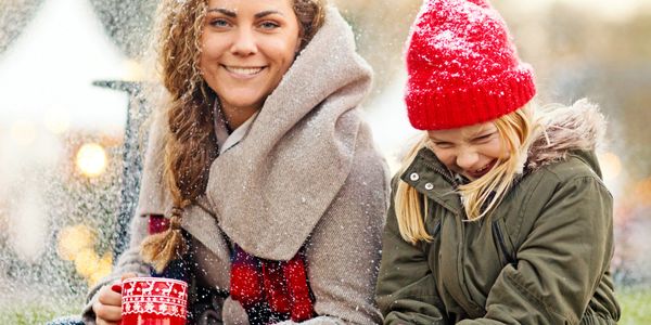 Smiling woman and child enjoying winter with hot drinks and snow.