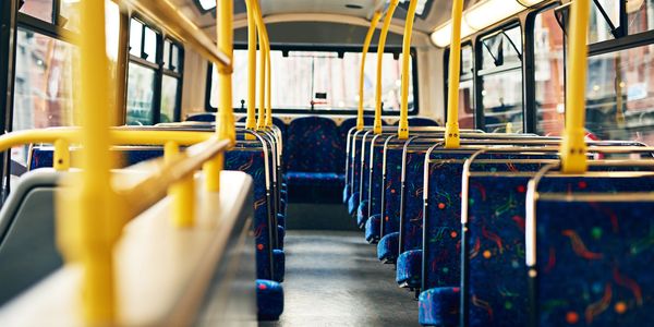 Empty interior of a bus with patterned seats and yellow railings.