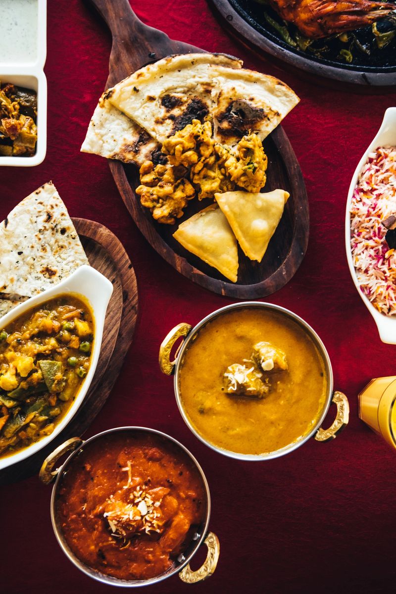 Indian feast with butter chicken, chicken tandoori, lamb curry, vegetable curry, samosas, pakoras, bhajis, naan bread and basmati rice on a table. North Indian food