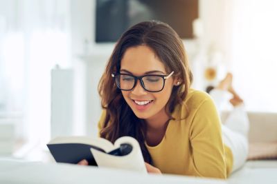 A woman with glasses reading a book and smiling.