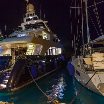 Two yachts docked side by side at night with lights reflecting on water.