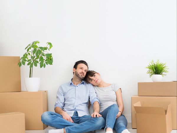 Couple resting on floor surrounded by moving boxes and plants.