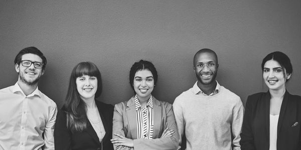 A diverse group of five professionals smiling against a blue wall.