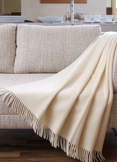 Cream-colored fringed throw blanket draped over a beige sofa in a cozy living room.