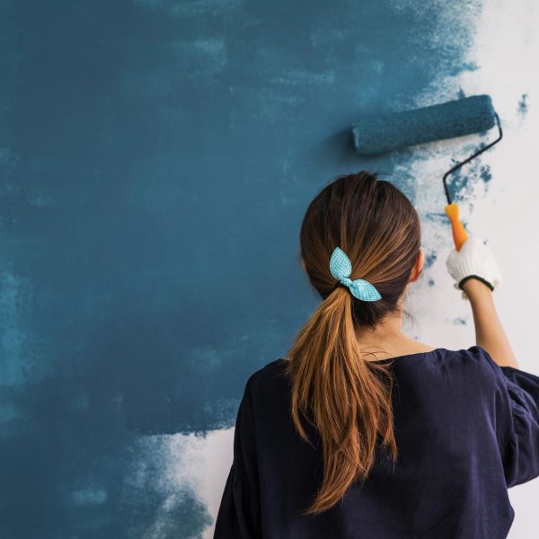 Woman painting wall with blue paint roller.