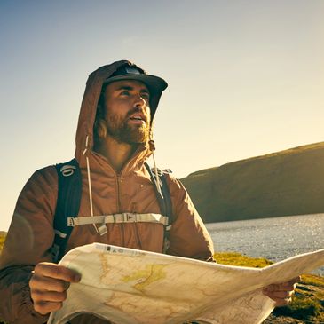Hiker studies a map near a lake at sunset.