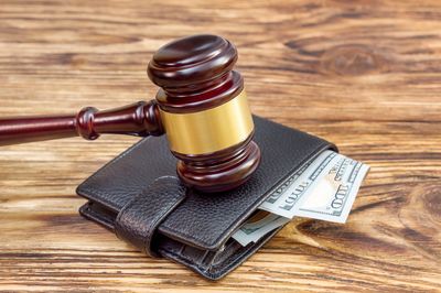 A judge's gavel rests on a wallet stuffed with cash on a wooden surface.