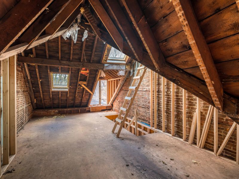 Interior of old victorian style house under renovation, attic floor with exposed roof. Framing stage inside. Sunny winter day on urban city street.