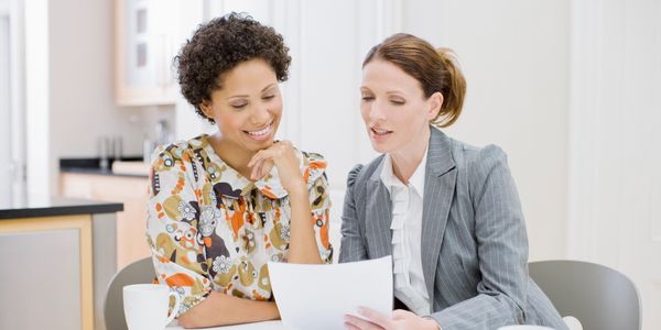 Two women reviewing documents together at a table in a bright room.