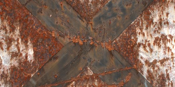 Close-up of heavily rusted metal with a large X-shaped reinforcement.
