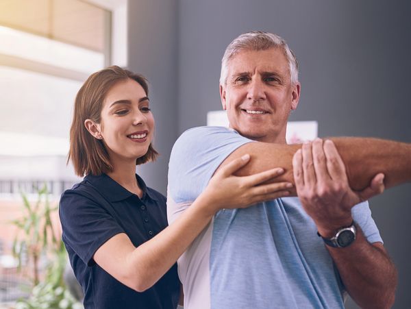 Physical therapist helping older man stretch his arm in a bright clinic.