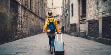 Person in a yellow jacket walking with a suitcase through a narrow stone street.