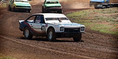 Vintage cars racing on a dirt track during a rally event.