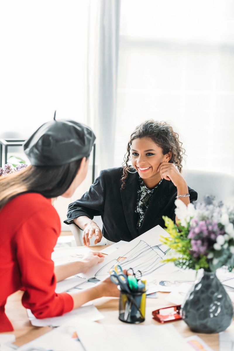 young multiethnic fashion designers smiling each other while working with sketches