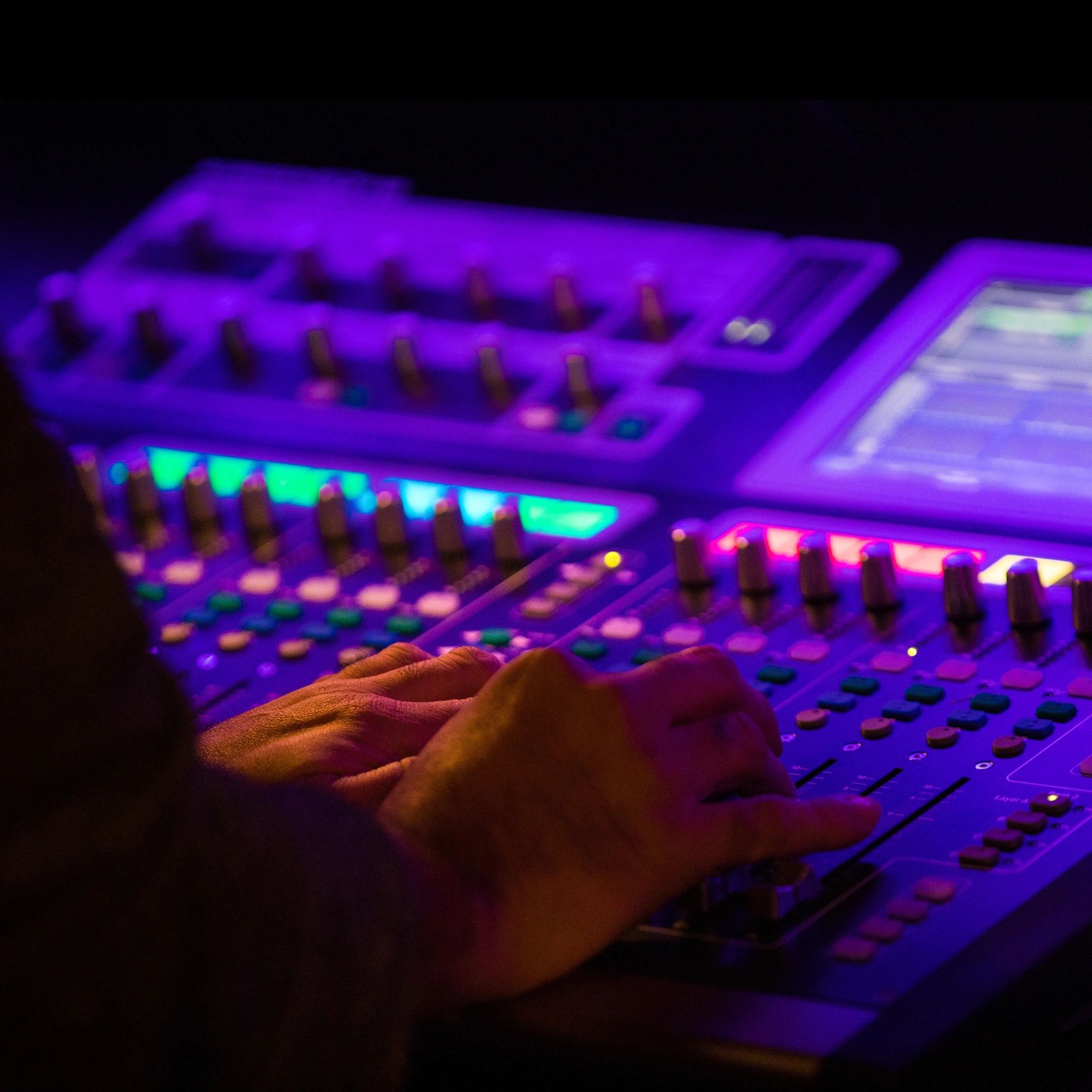 Hands adjusting controls on a colorful audio mixing console.