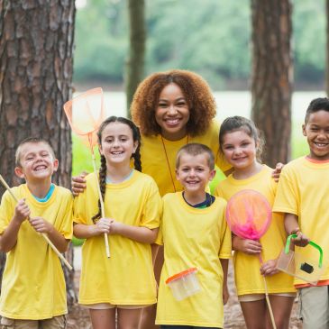 Happy kids and teacher in yellow shirts outdoors with nets and containers.