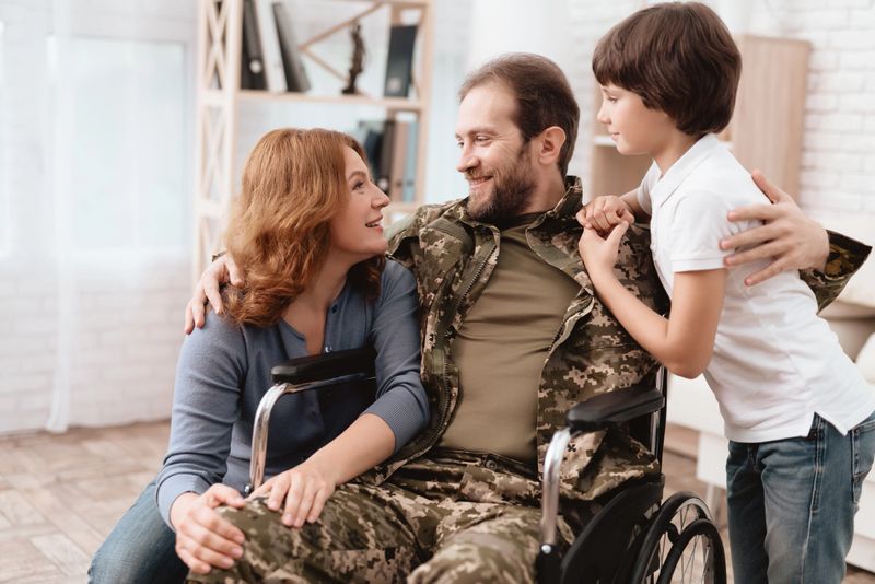 The veteran in a wheelchair came back from the army. Wife and son are glad to see him. A man in uniform in a wheelchair with his family.