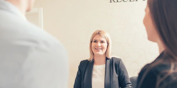 A receptionist smiling while assisting two guests at a reception desk.