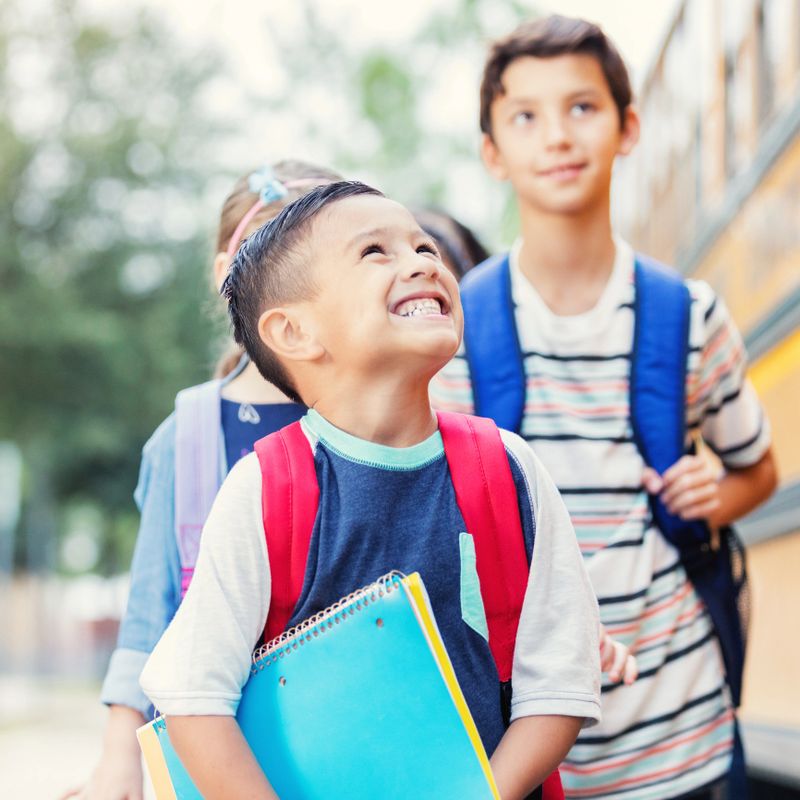 Happy mixed race schoolboy smiles up at the school bus driver as he boards the school bus. He is excited about the first day of school.