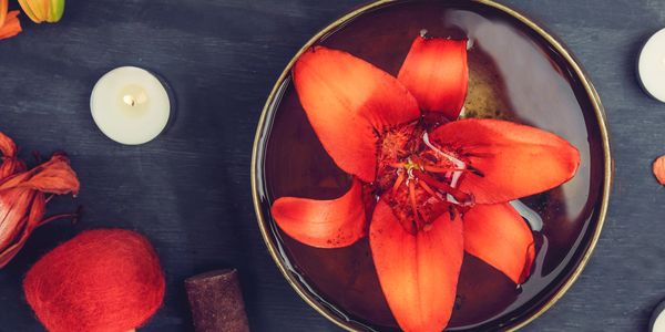 Vibrant red flower floating in water with candles and decorative items.