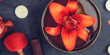 Bright orange flower floating in a bowl of water surrounded by candles and spices.